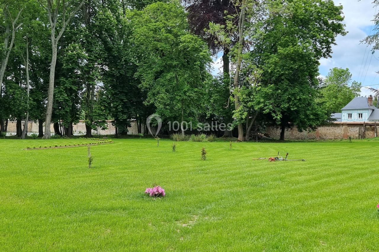 Pelouse verdoyante avec quelques fleurs dispersées, entourée d'arbres et d'un mur en pierre au fond.