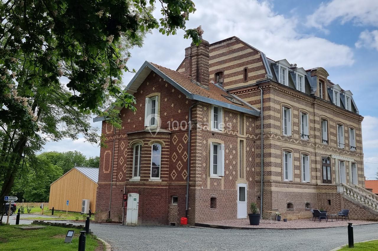 Bâtiment en briques rouges et beiges avec des détails architecturaux, entouré de verdure et d'un ciel partiellement nuageux.
