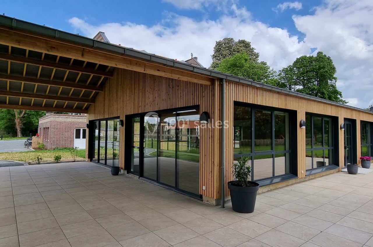 Bâtiment moderne en bois avec de grandes baies vitrées, entouré d'une terrasse en dalles et d'un jardin verdoyant.