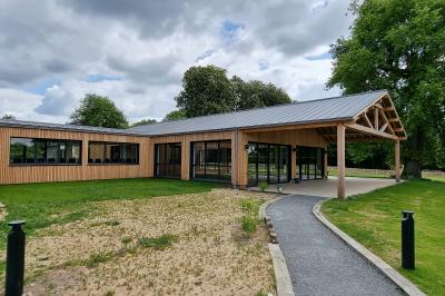 Des chèvres se tiennent près d'une clôture dans un champ herbeux entouré de barrières en bois.