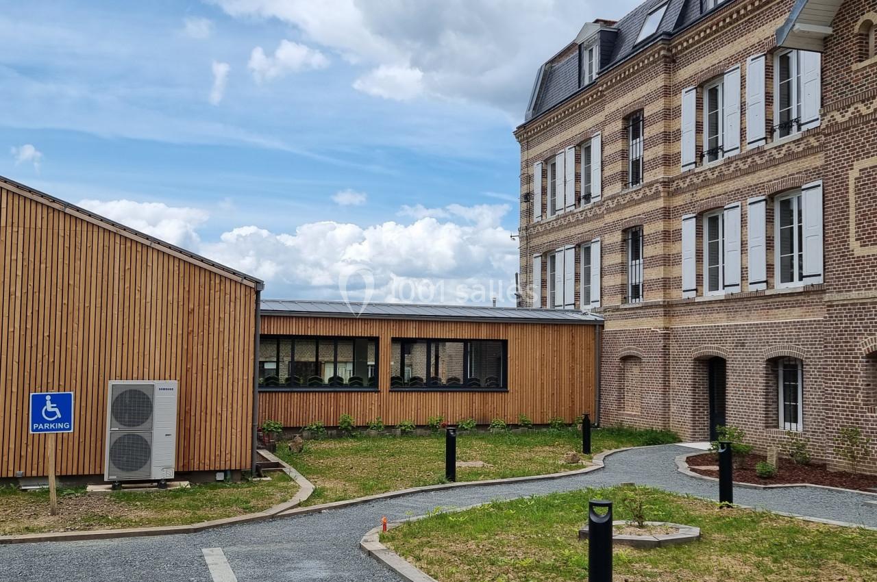 Bâtiment en briques et bois avec un chemin accessible et un panneau signalant un stationnement pour personnes handicapées.