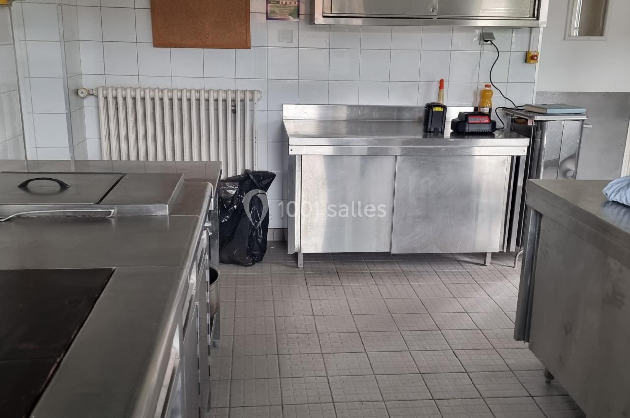 Cuisine professionnelle avec plans de travail en acier inoxydable, plaques de cuisson et murs carrelés blancs.