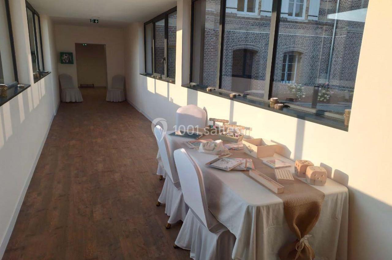 Table décorée avec des objets artisanaux dans un couloir lumineux avec parquet et grandes fenêtres donnant sur un bâtiment…
