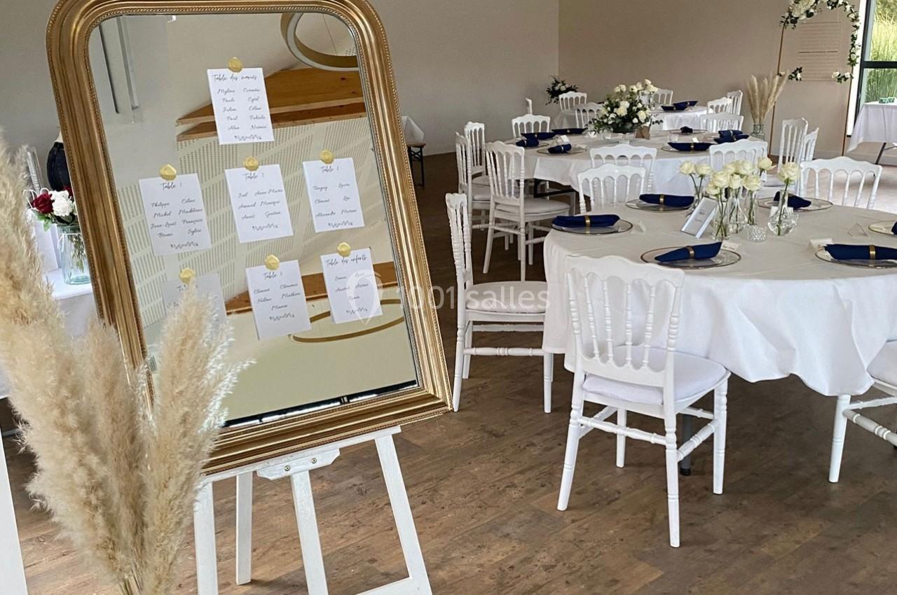 Plan de table affiché sur un miroir doré, entouré de décorations florales, dans une salle de réception élégante.