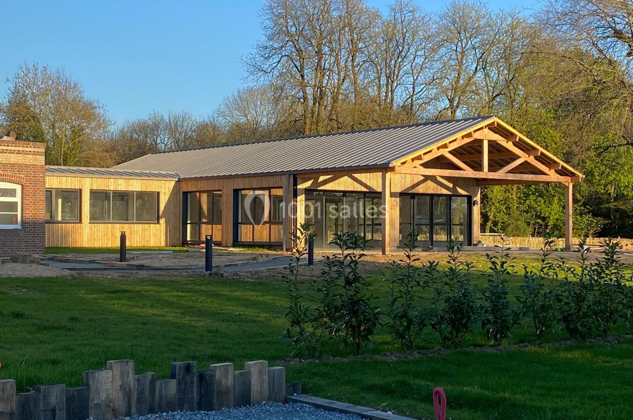 Bâtiment moderne en bois avec de grandes baies vitrées, entouré de verdure et éclairé par une lumière naturelle.