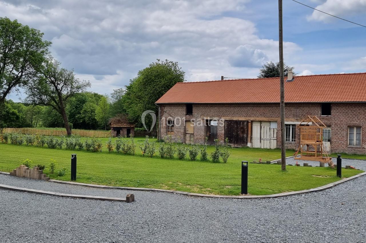 Bâtiment en briques avec toit en tuiles rouges, entouré d'un jardin, d'une pelouse et d'une allée en gravier.