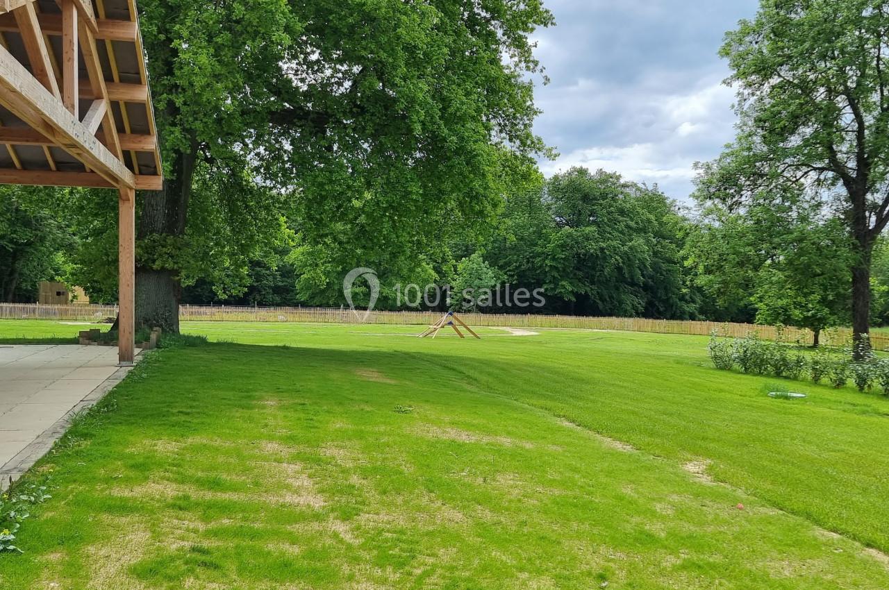 Vue d'un grand jardin verdoyant avec pelouse, arbres et une structure en bois sur la gauche.