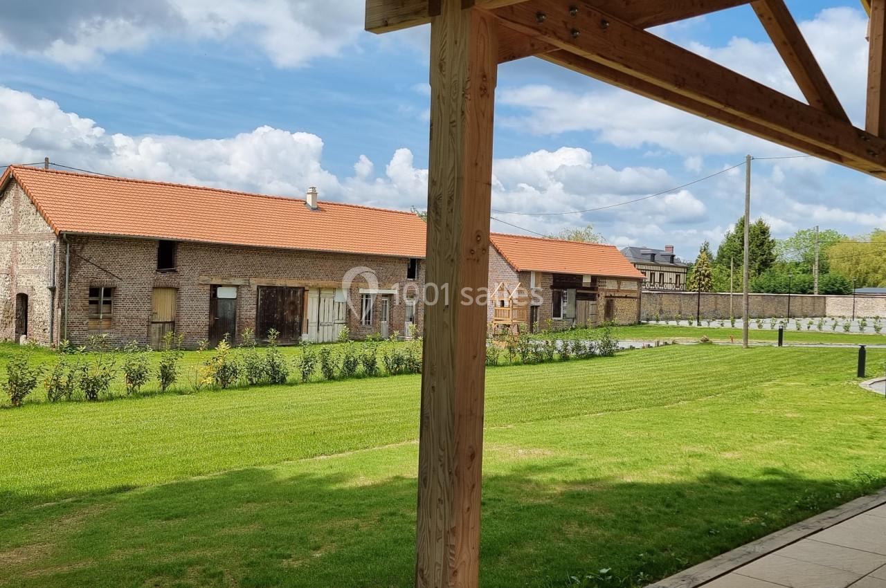 Vue d'un bâtiment en briques rouges avec toit en tuiles, entouré d'une pelouse et d'arbustes, sous un ciel partiellement…