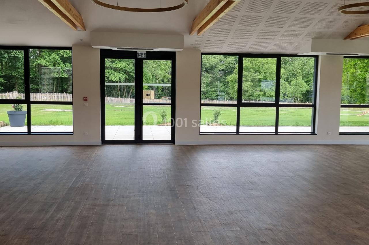 Salle lumineuse avec parquet, grandes baies vitrées donnant sur un espace extérieur verdoyant.