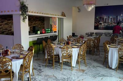 Salle de réception élégante avec tables dressées, chaises dorées, bar en arrière-plan et décoration lumineuse.