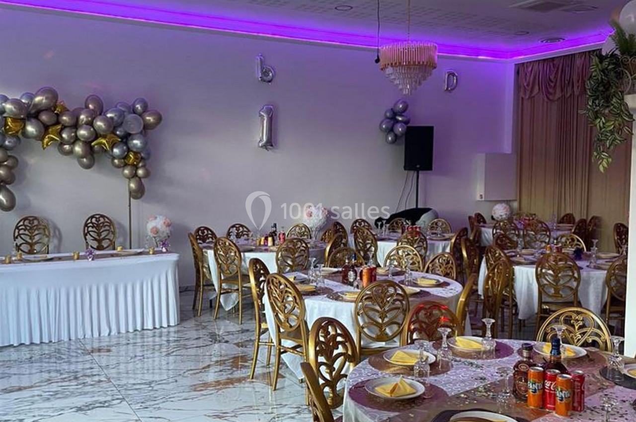 Salle de réception décorée avec des ballons, des tables dressées et un éclairage violet au plafond.