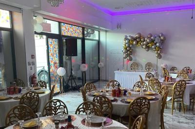 Salle de réception élégante avec tables dressées, chaises dorées, bar en arrière-plan et décoration lumineuse.