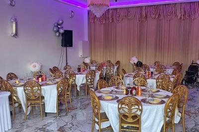 Salle de réception élégante avec tables dressées, chaises dorées, bar en arrière-plan et décoration lumineuse.