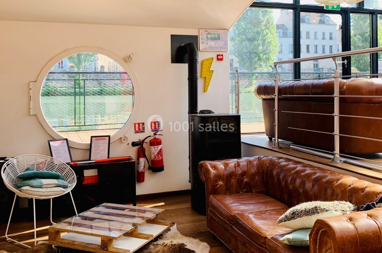 Espace intérieur lumineux avec canapé en cuir, table basse, fauteuil et grande fenêtre ronde donnant sur l'extérieur.