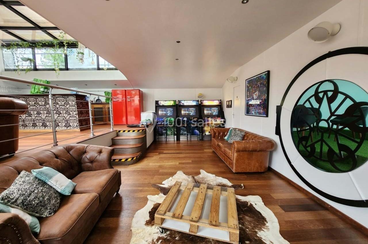 Salon lumineux avec canapés en cuir, tapis en peau, table basse en bois et coin rétro avec bornes d'arcade.