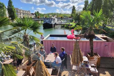 Groupe de personnes réunies dans un bar extérieur animé avec terrasse, palmiers et guirlandes lumineuses.