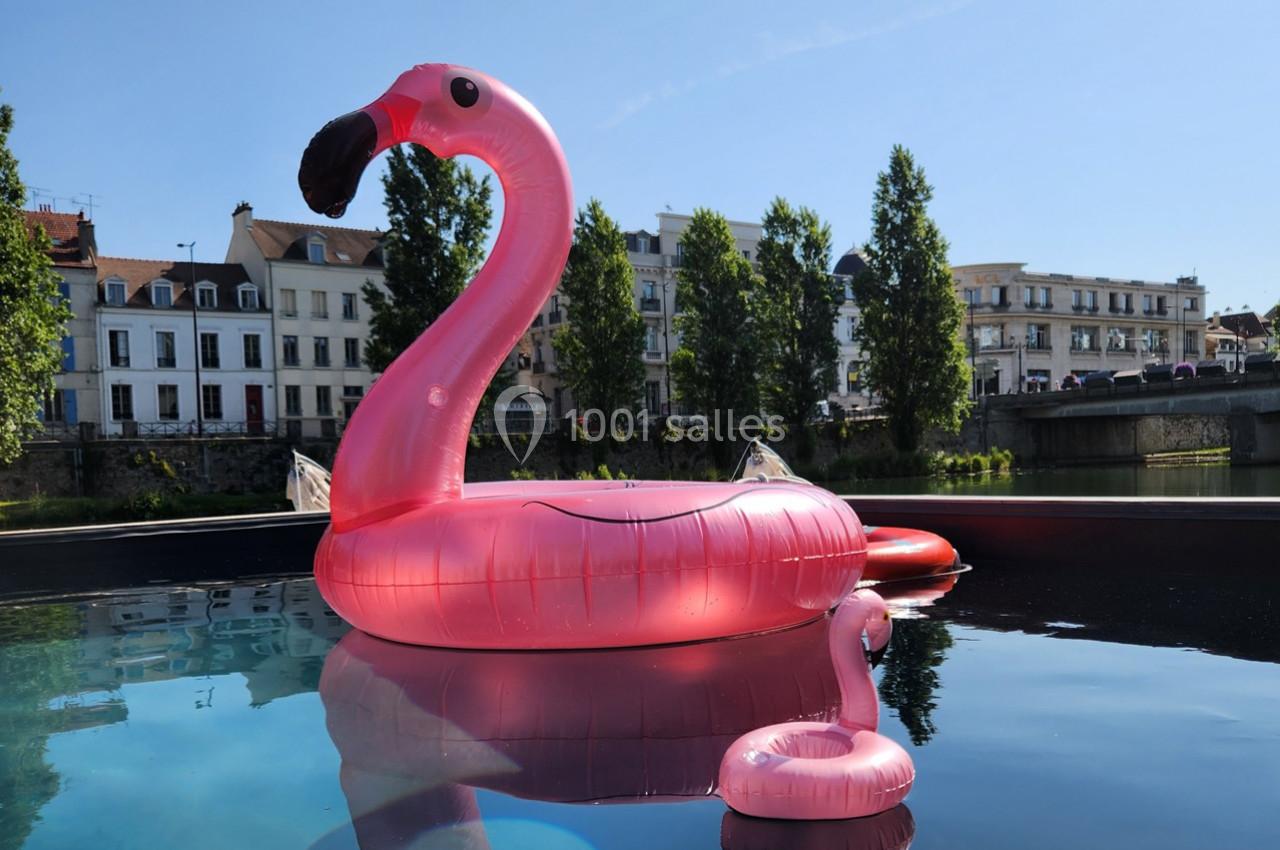 Flamants roses gonflables flottant sur une piscine, avec des bâtiments et des arbres en arrière-plan.