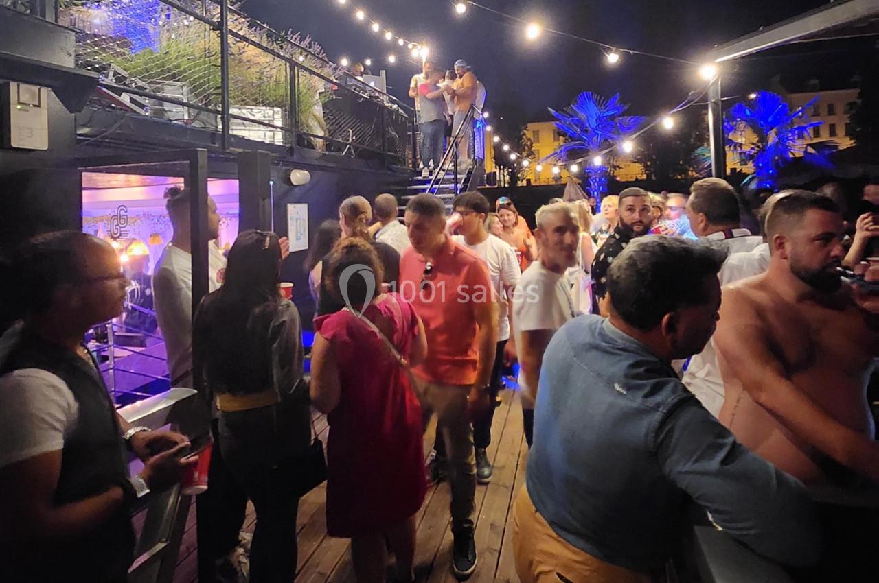 Groupe de personnes discutant et socialisant sur une terrasse éclairée par des guirlandes lumineuses, en soirée.