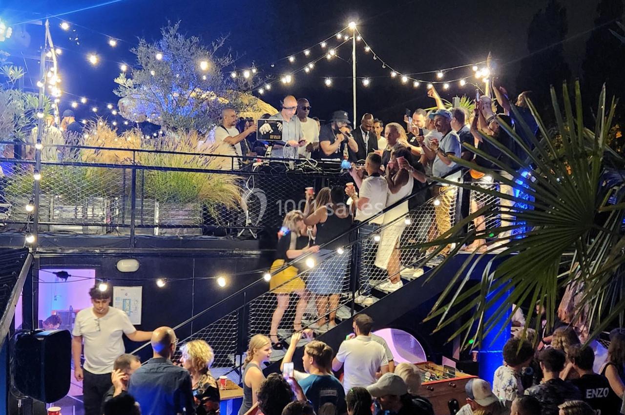 Foule dansant et socialisant sur une terrasse illuminée par des guirlandes lumineuses lors d'une soirée en plein air.