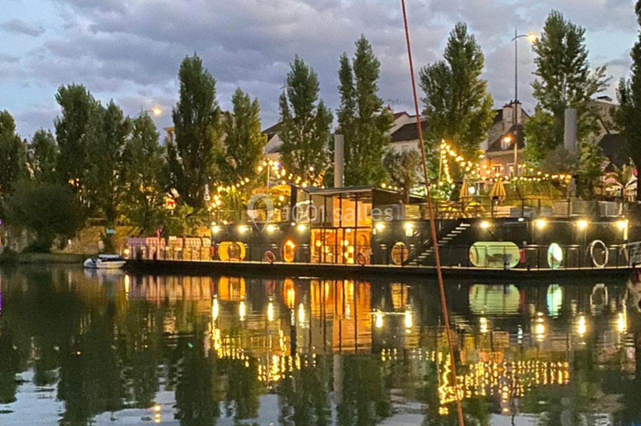 Reflet d'un bâtiment illuminé et entouré d'arbres sur une étendue d'eau au crépuscule.