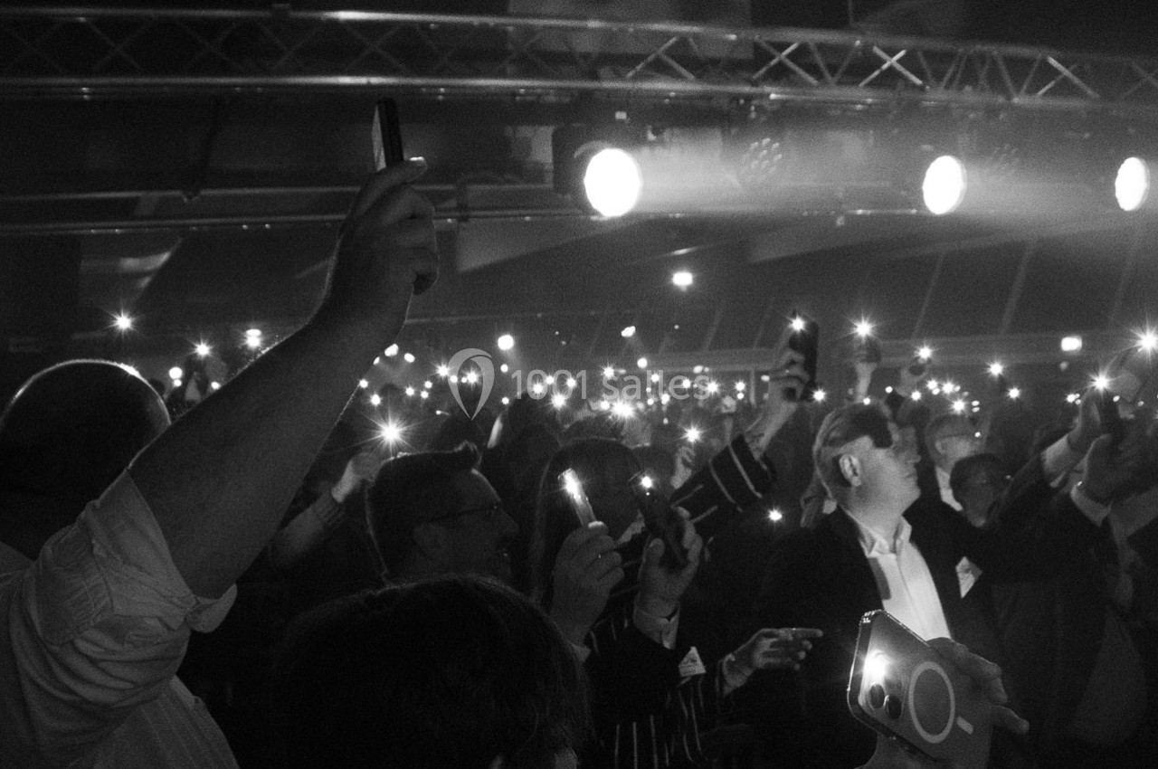 Groupe de personnes dans une salle sombre levant leurs téléphones allumés vers le plafond.