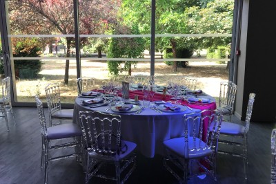Salle de réception décorée avec des tables rondes, nappes blanches, chemins de table roses et chaises transparentes.
