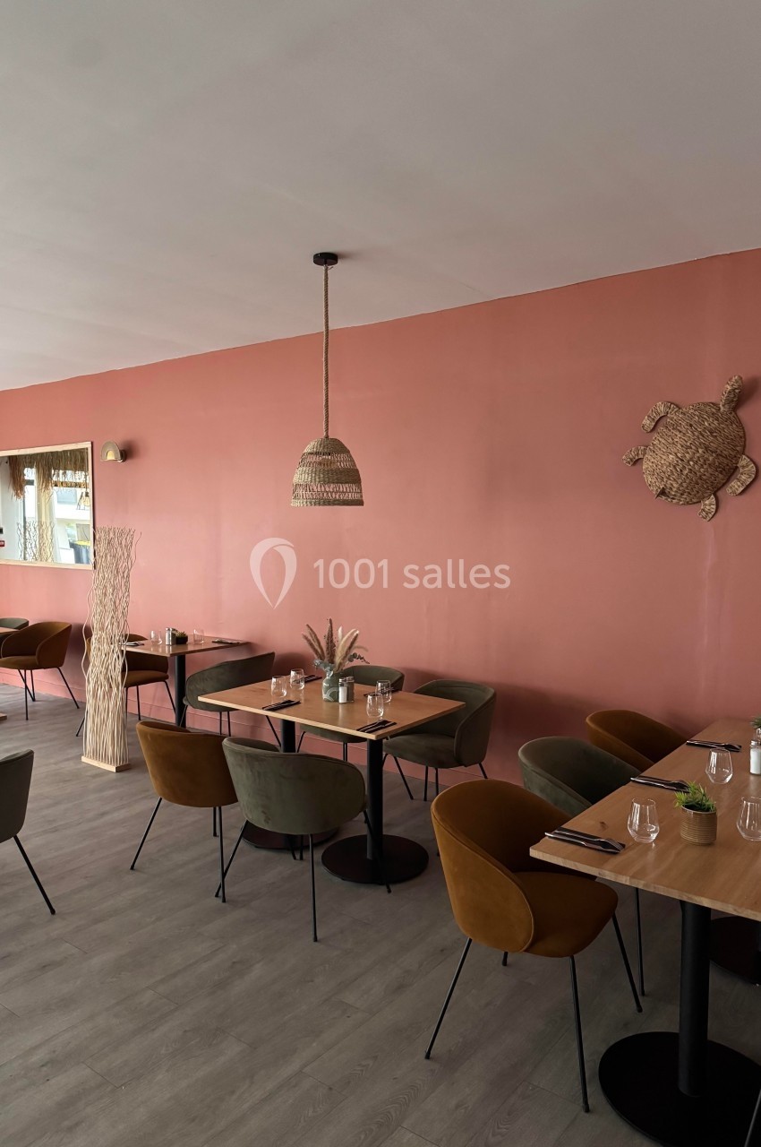 Salle de restaurant avec murs rose saumon, tables en bois, chaises colorées et décoration murale en osier.