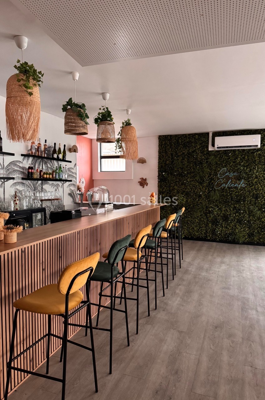 Bar moderne avec comptoir en bois, tabourets colorés, suspensions en osier, mur végétal et étagères à bouteilles.