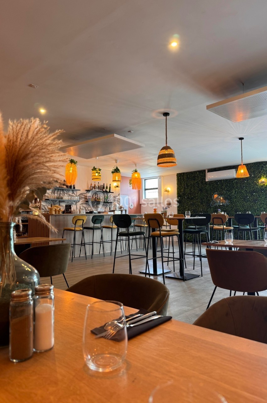Salle de restaurant moderne avec tables en bois, chaises design, éclairage chaleureux et mur végétal en arrière-plan.