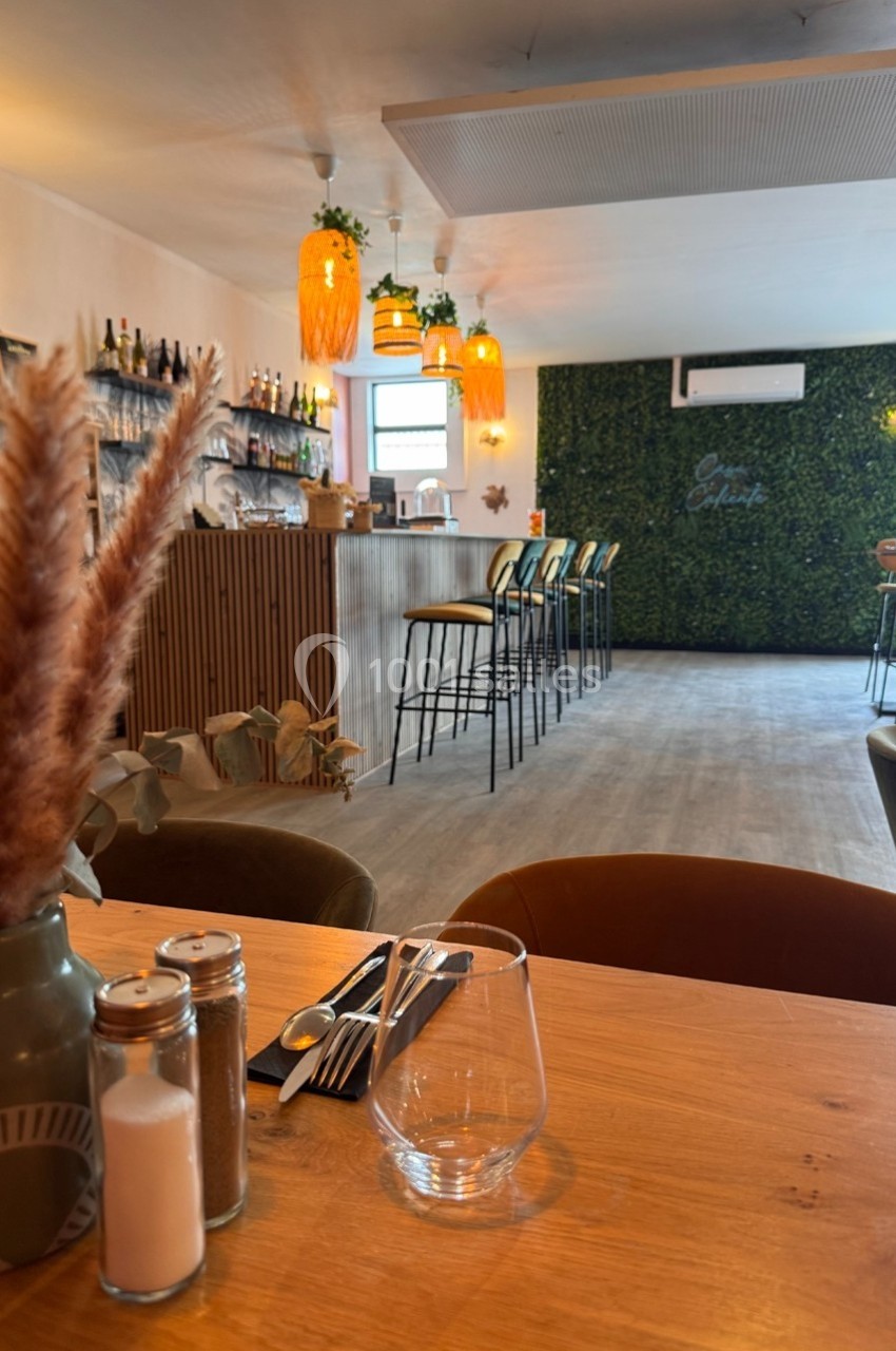 Salle de restaurant lumineuse avec un mur végétal, un bar en bois, et une table dressée au premier plan.