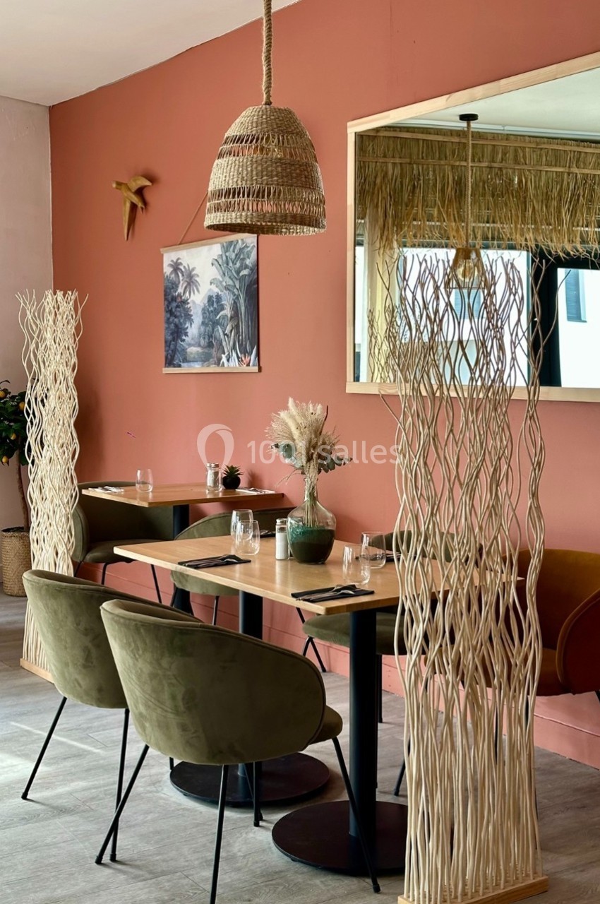 Salle de restaurant décorée avec des tons naturels, des chaises en velours, des séparateurs en bois et un mur rose.
