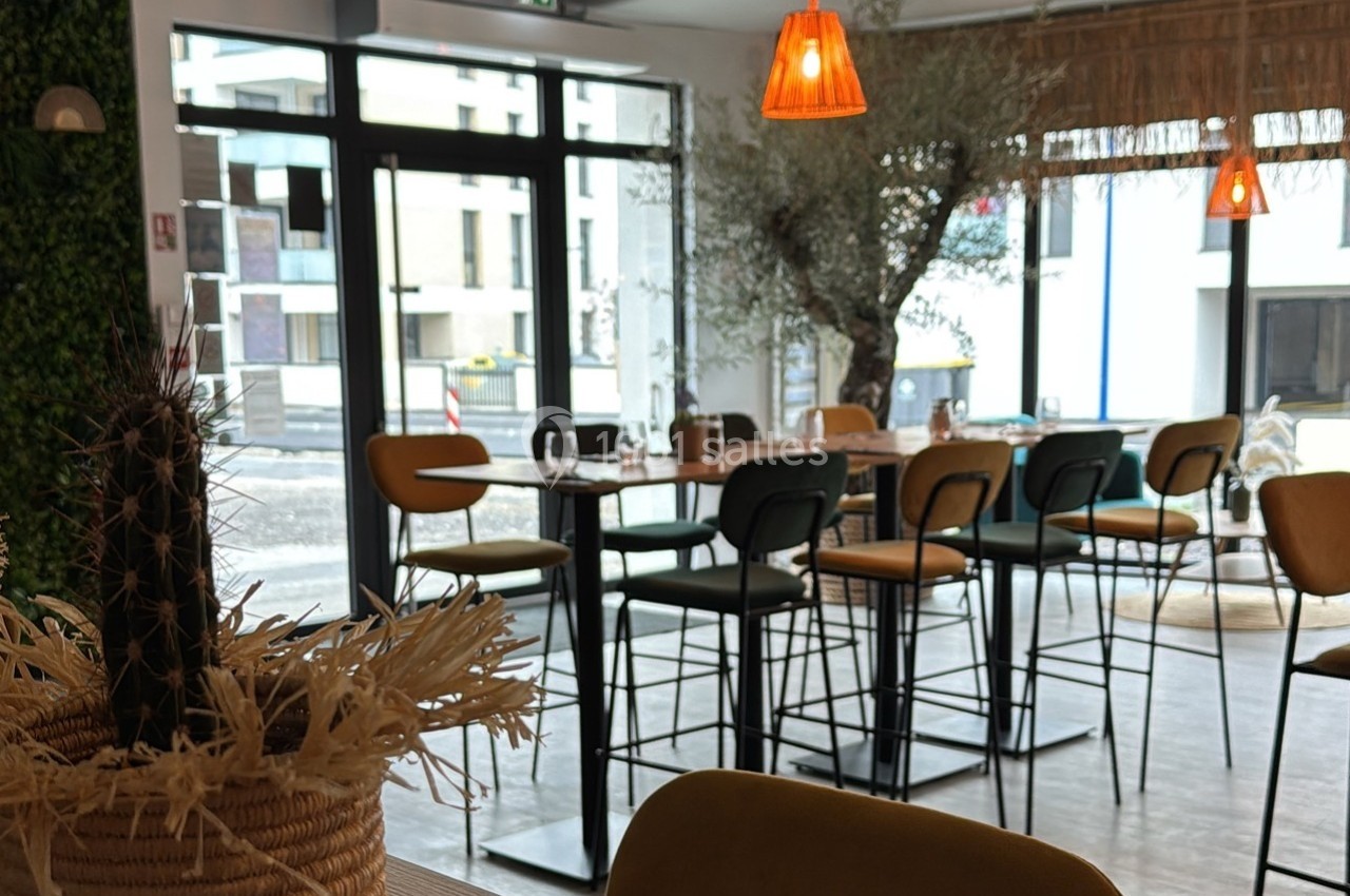 Salle de restaurant lumineuse avec des tables hautes, des chaises modernes et une décoration végétale.