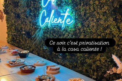 Table en bois avec deux chaises vertes, décorée d'un tableau tropical et séparée par un paravent en branches.