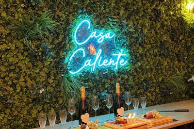 Table en bois avec deux chaises vertes, décorée d'un tableau tropical et séparée par un paravent en branches.