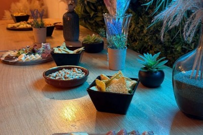 Table en bois avec deux chaises vertes, décorée d'un tableau tropical et séparée par un paravent en branches.