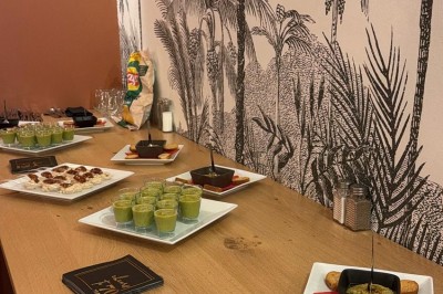 Table en bois avec deux chaises vertes, décorée d'un tableau tropical et séparée par un paravent en branches.