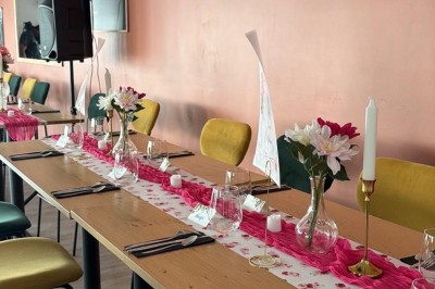 Table en bois avec deux chaises vertes, décorée d'un tableau tropical et séparée par un paravent en branches.