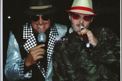 Des artistes en costumes brillants dansent sur une scène illuminée par des projecteurs colorés et un écran lumineux.