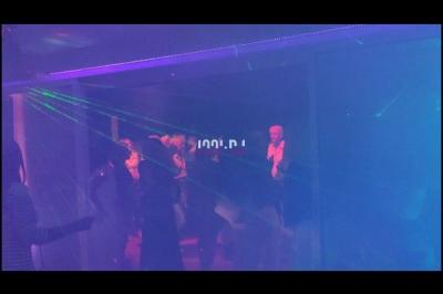 Des artistes en costumes brillants dansent sur une scène illuminée par des projecteurs colorés et un écran lumineux.