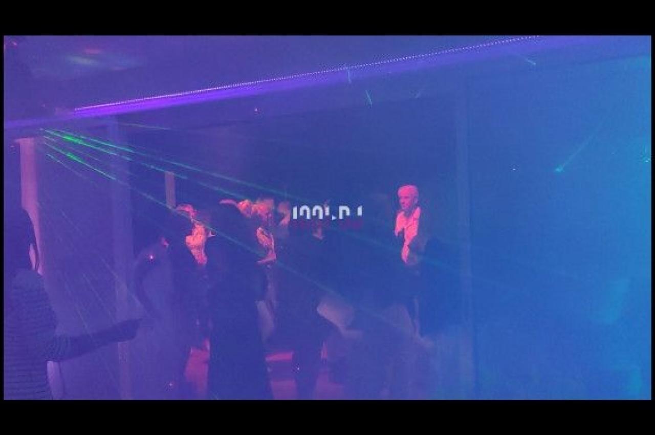 Personnes dansant dans une ambiance sombre avec des lumières laser colorées.