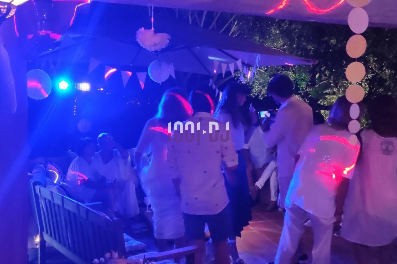 Groupe de personnes en tenue blanche dans une soirée festive avec éclairage coloré et décorations suspendues.