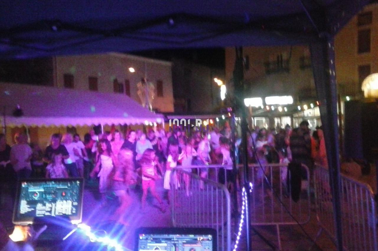 Foule dansante en soirée en plein air, vue depuis une table de mixage avec éclairages colorés.