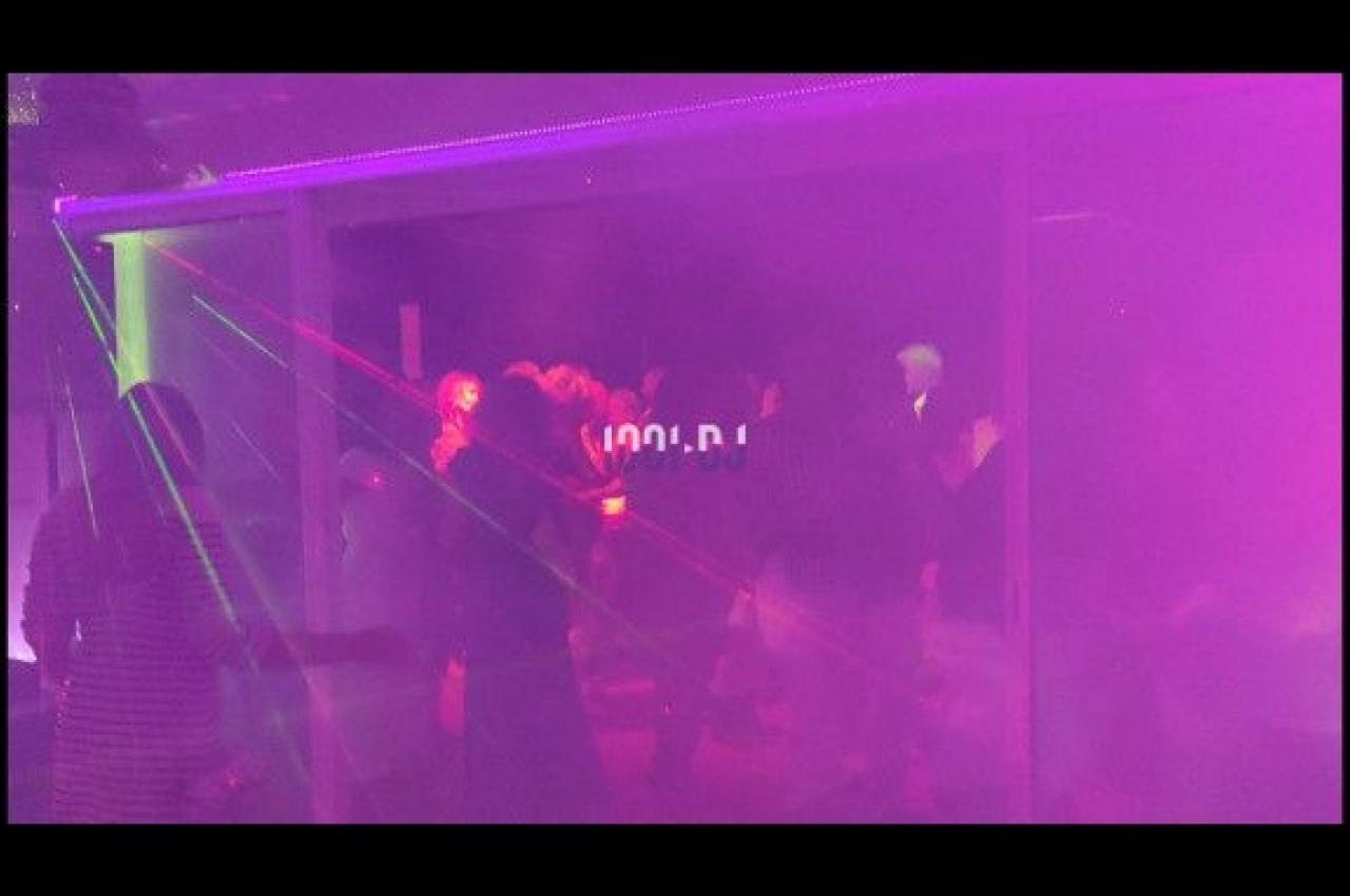 Personnes dansant dans une ambiance sombre avec des lumières laser colorées et une atmosphère enfumée.