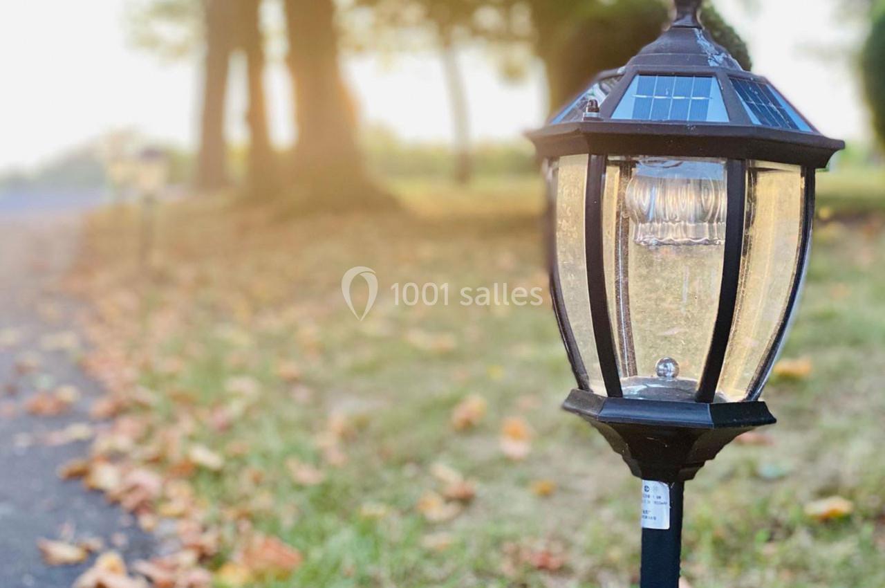 Lampe solaire de jardin en gros plan, éclairant un chemin bordé de feuilles mortes dans un parc au coucher du soleil.