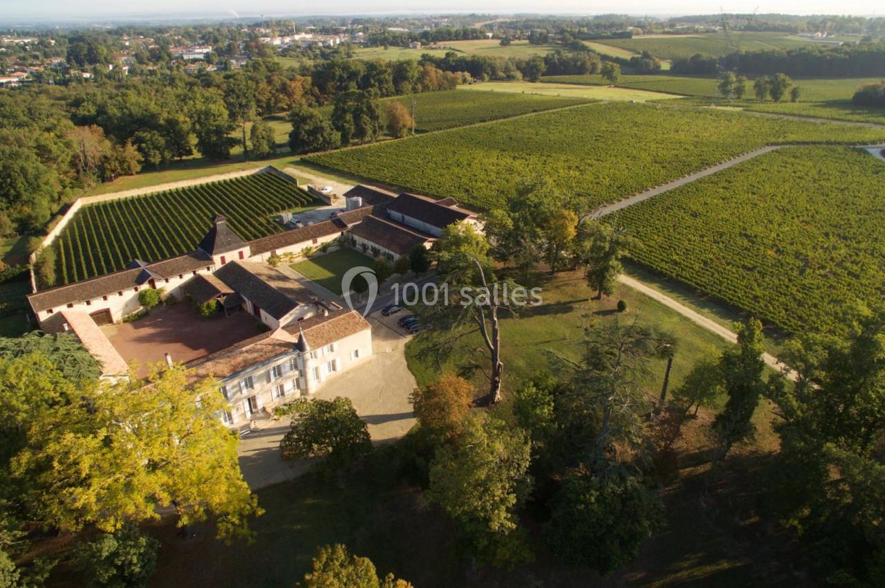 Vue aérienne d'un domaine viticole entouré de vignes, avec des bâtiments en pierre et des arbres environnants.