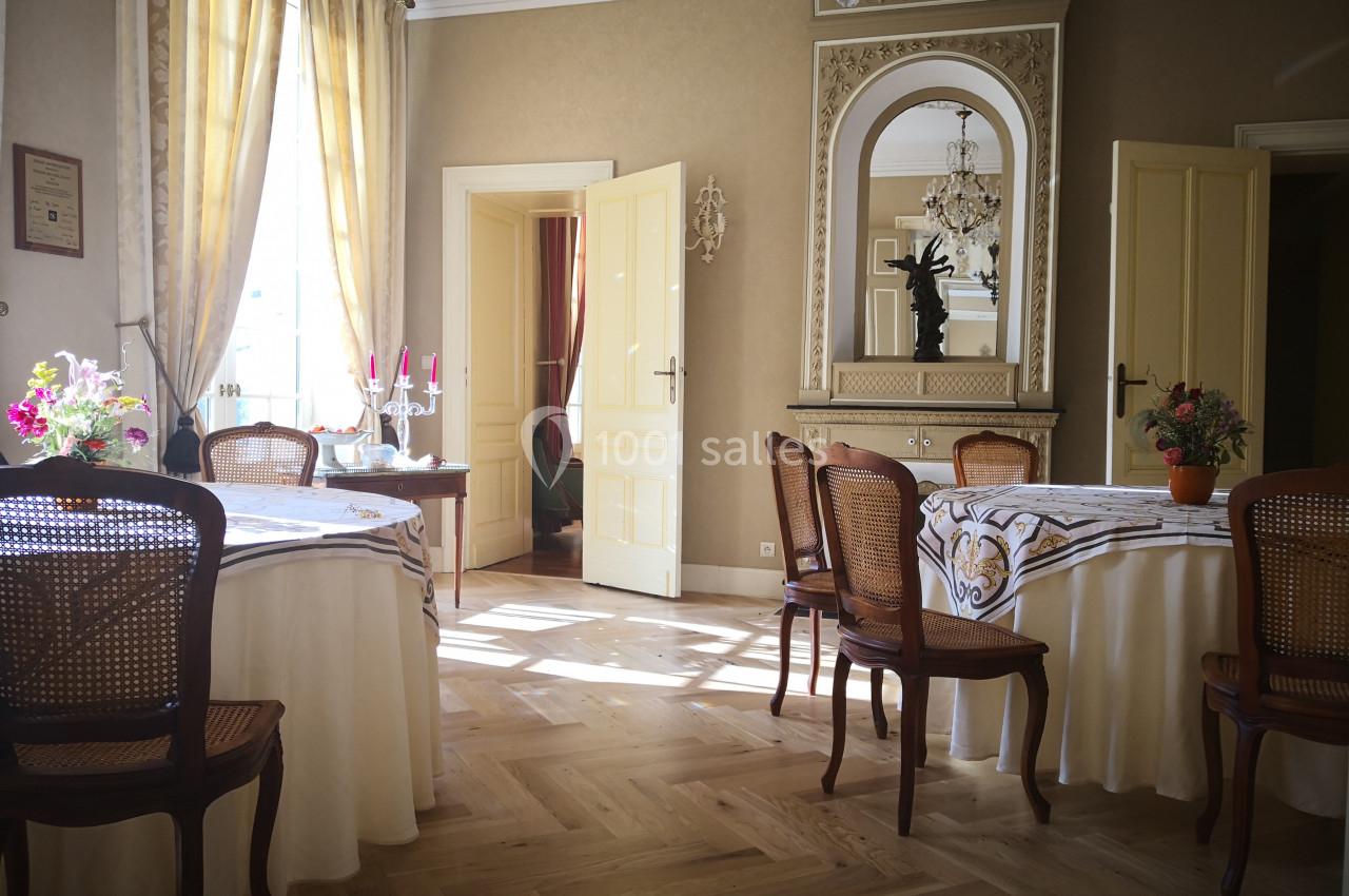 Salle lumineuse avec parquet en bois, tables rondes dressées, chaises en rotin et cheminée ornée d'un miroir.