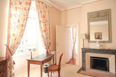 Chambre lumineuse avec murs en toile de Jouy rouge, mobilier classique, table basse et fauteuils près d'une fenêtre.
