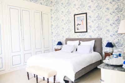 Chambre lumineuse avec murs en toile de Jouy rouge, mobilier classique, table basse et fauteuils près d'une fenêtre.