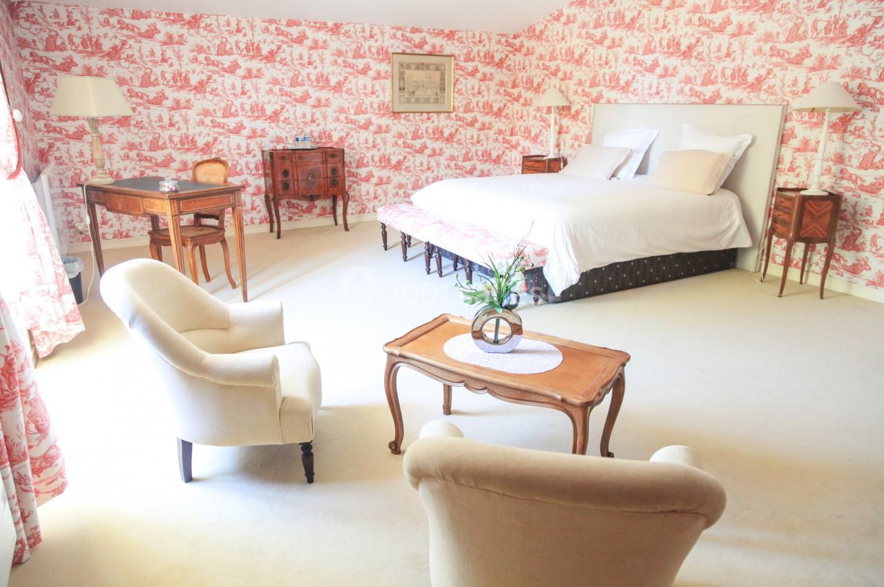 Chambre lumineuse avec lit double, fauteuils, table basse et mobilier en bois, décorée de papier peint rouge et blanc.