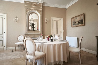 Chambre lumineuse avec murs en toile de Jouy rouge, mobilier classique, table basse et fauteuils près d'une fenêtre.